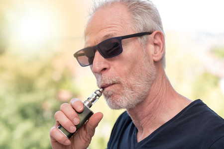 Portrait of mature man smoking an electronic cigarette, light effectの写真素材