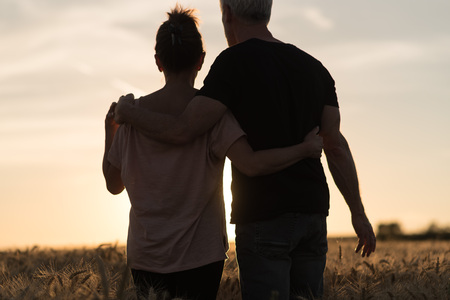 Couple walking together in a wheat field on summer evening, sunlight effectの写真素材