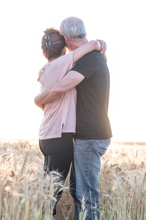 Senior couple embracing each other in a wheat field at sunset, sunlight effectの写真素材
