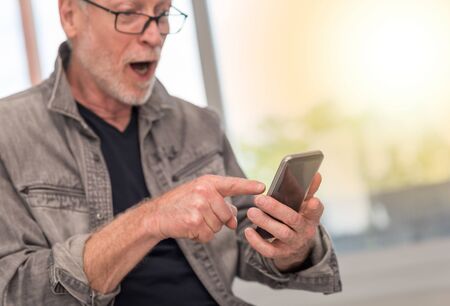 Surprised mature man looking at his mobil phone, light effectの写真素材