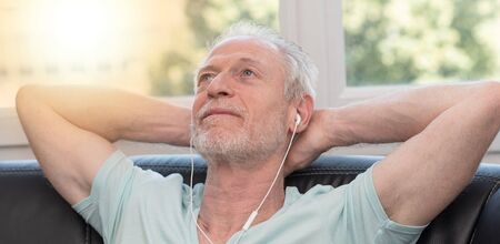 Portrait of mature man listening music with earphones at home, light effectの写真素材