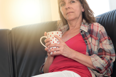 Thoughtful mature woman sitting on sofa, light effectの写真素材
