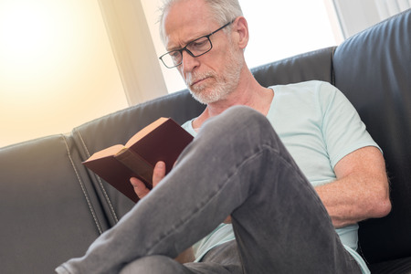 Portrait of mature man reading a book at home, light effect