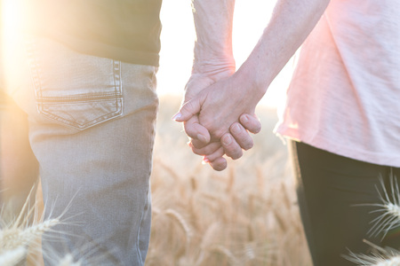 Couple holding hands in a wheat field on a summer evening at sunset, sunlight effectの写真素材