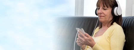 Modern mature woman listening music on mobile phone at home