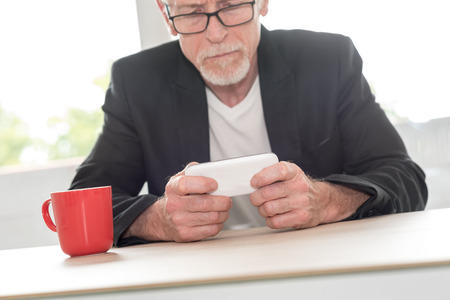 Senior man using his phone at homeの写真素材