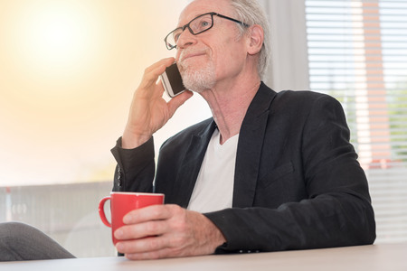 Senior man talking on phone at home, light effectの写真素材