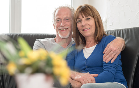Portrait of a happy senior couple sitting on sofa and embracing each otherの写真素材