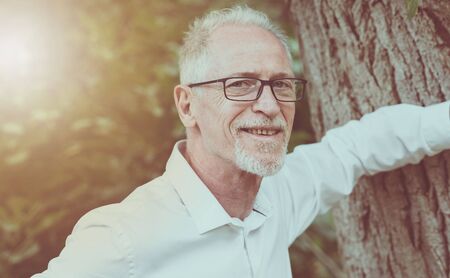 Portrait of happy mature man with an arm against a tree, light effectの写真素材