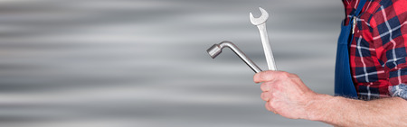 Arm of mechanic holding wrenchs on blurred background