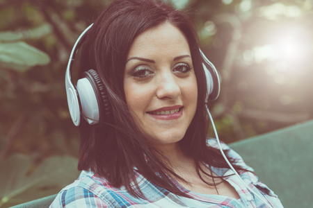Pretty young woman listening to music with headphones, outdoors, light effectの写真素材