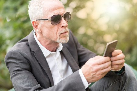 Mature man using his mobile phone outdoors, light effectの写真素材