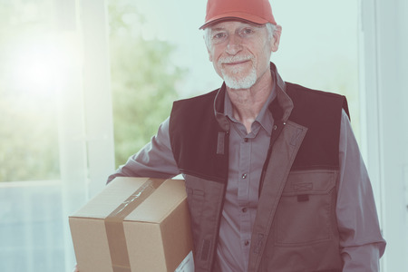 Portrait of smiling senior deliverer holding a packageの写真素材