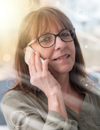 Mature woman talking on mobile phone, overlaid with network, light effectの写真素材