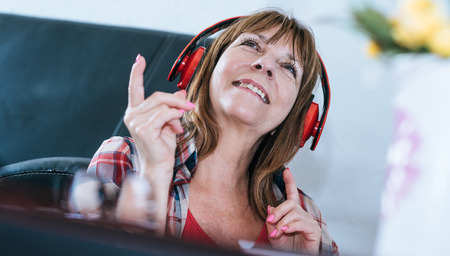 Happy mature woman listening to music at home