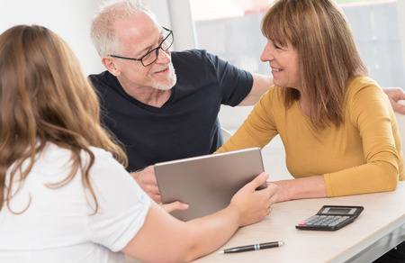 Real estate agent giving explanations on tablet to senior coupleの写真素材