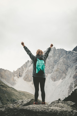 Back view of woman with arms raised standing on peak of rockの写真素材