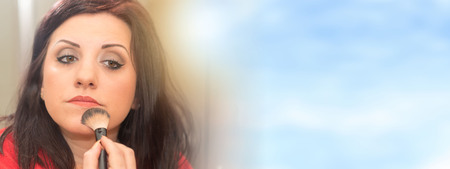 Beautiful brunette applying cosmetic powder on her faceの写真素材