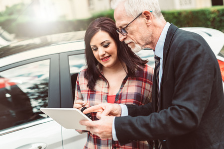 Car salesman giving explanations on tablet to pretty young woman, light effectの写真素材