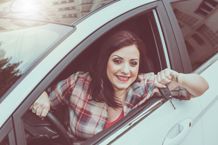 Smiling pretty woman sitting in new car and showing car keysの写真素材