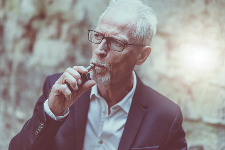 Portrait of mature man smoking electronic cigarette, light effectの写真素材
