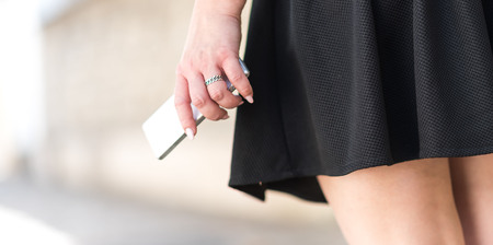 Young woman in black skirt with mobile phone in her hand outdoorsの写真素材