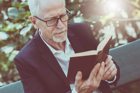 Mature man reading a book outdoors, light effectの写真素材