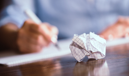 Person writing on notebook with crumpled sheet on table, focus on foregroundの写真素材