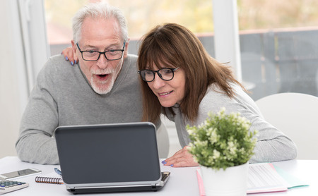 Happy mature couple having an amazing surprise on laptopの写真素材