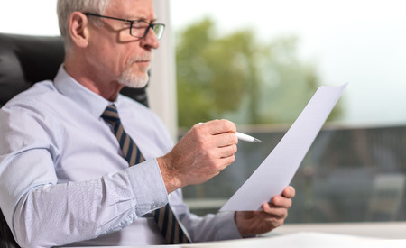 Portrait of mature businessman checking a document in officeの写真素材