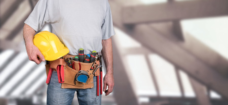 Building worker with tool belt and helmet on a construction site background
