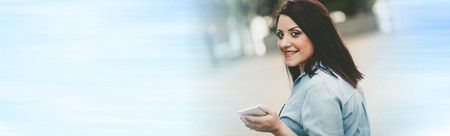 Portrait of happy young woman holding her mobile phone outdoors