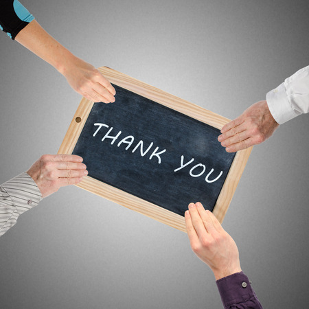 Word thank you written on chalkboard held by four handsの写真素材