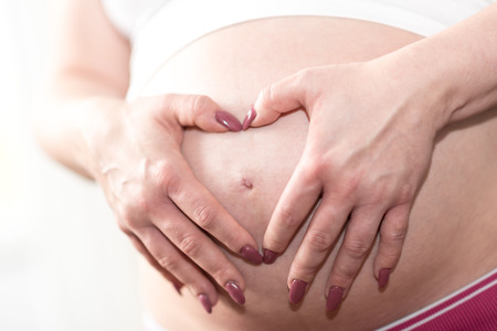 Pregnant woman holding hands in a heart shape on her belly