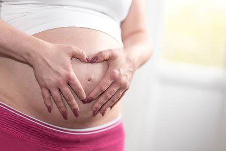 Pregnant woman holding hands in a heart shape on her belly