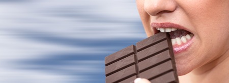 Close up of woman biting in a chocolate bar on blurred background