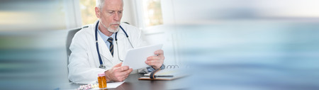 Senior doctor using tablet in office on blurred backgroundの写真素材
