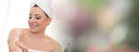 Portrait of smiling young woman applying moisturizing cream on her armの写真素材