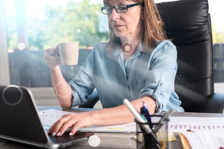 Portrait of mature businesswoman working on laptop in office, light effectの写真素材