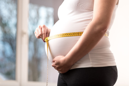 Pregnant woman measuring her belly with tape measureの写真素材
