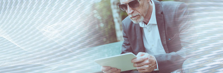 Mature man sitting outdoors and using his tablet. panoramic bannerの写真素材
