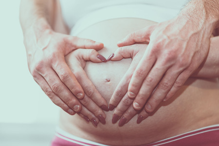 Couple holding hands in a heart shape on pregnant belly