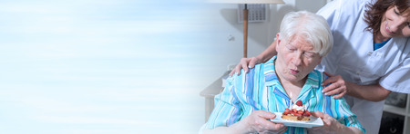 Senior woman blows out a birthday cake candle. panoramic bannerの写真素材