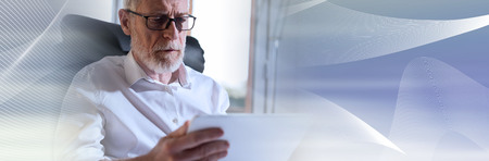 Senior businessman using a digital tablet in office, hard light. panoramic bannerの写真素材
