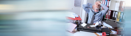 Overworked businessman sitting at a messy desk in office. panoramic bannerの写真素材