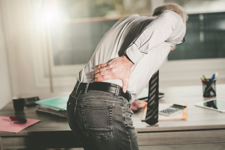 Businessman suffering from back pain in office, light effect