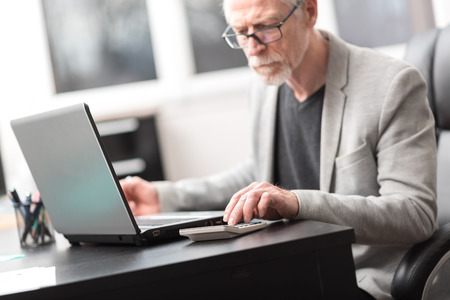 Mature businessman using calculator at officeの写真素材