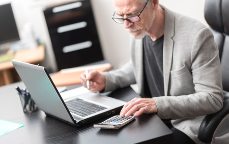 Mature businessman using calculator at officeの写真素材