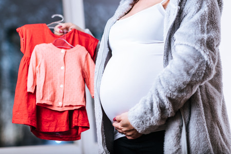 Pregnant woman holding baby clothes and touching her belly