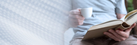 Man reading a book and holding a cup of coffee. panoramic banner